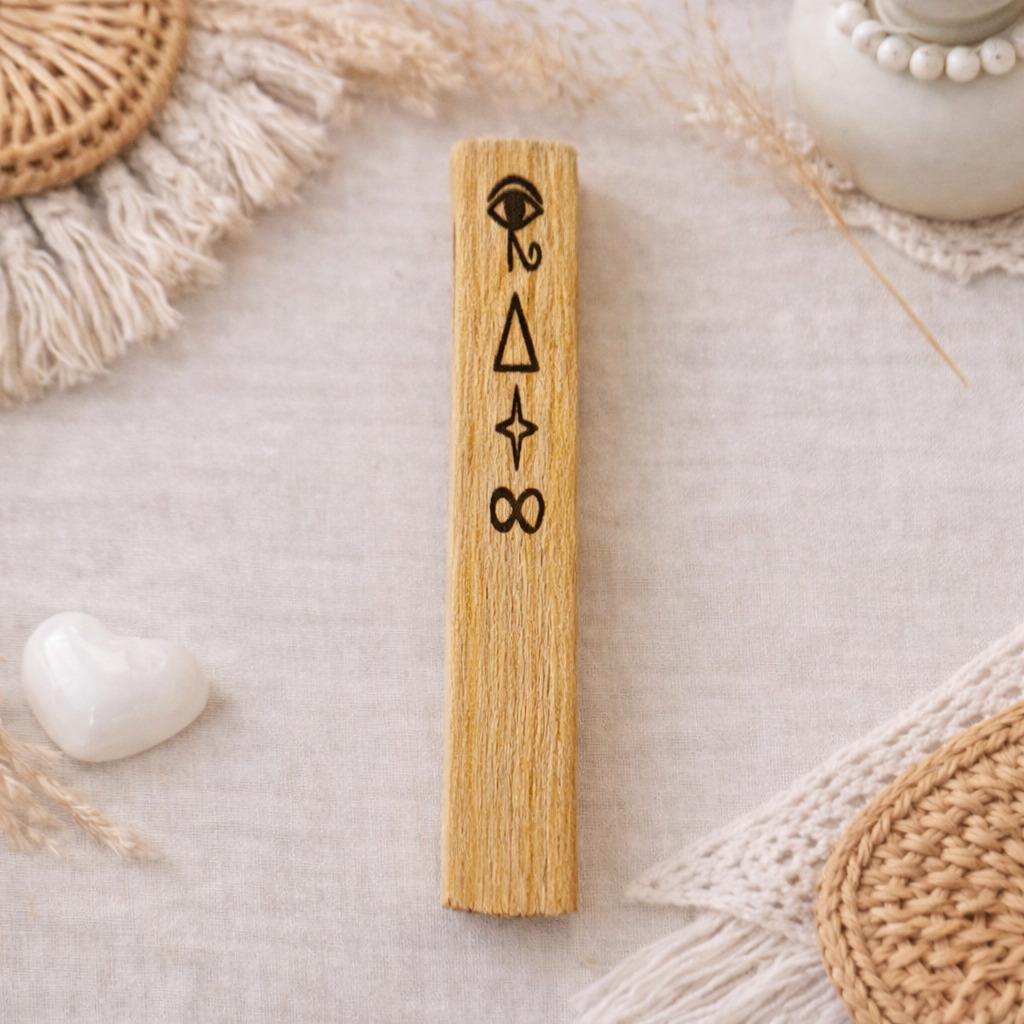 Bâton en Palo Santo gravé de symboles représentant la clairvoyance, photographié dans une ambiance naturelle et bohème